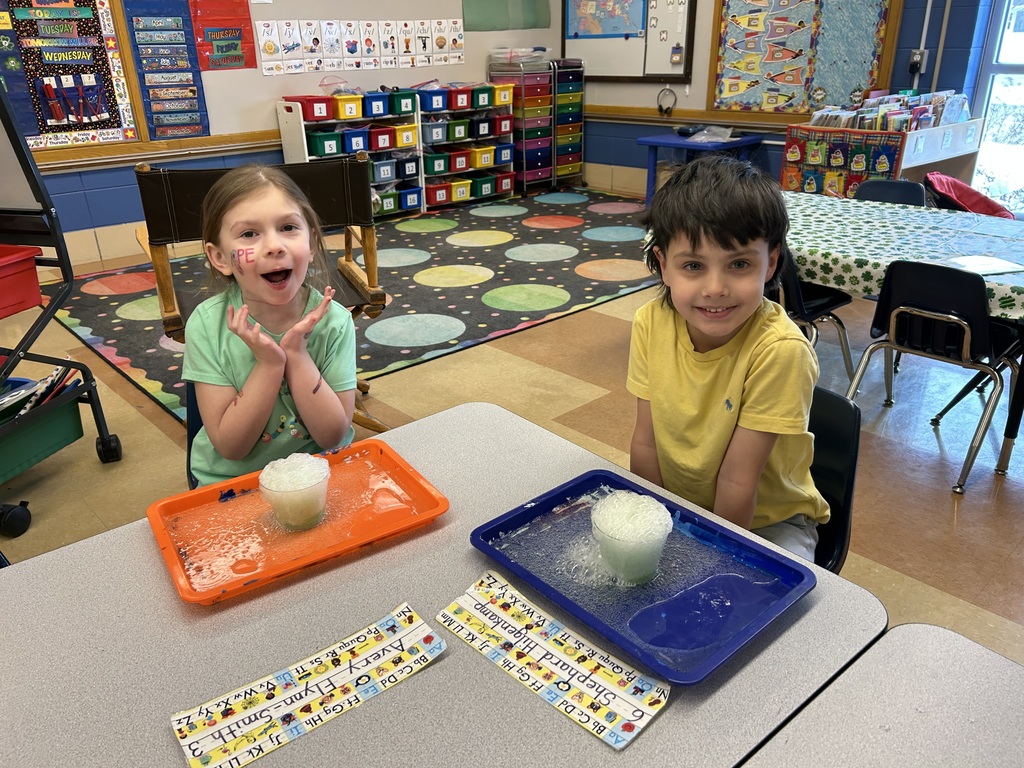 students watching a science experiment with a cup of bubbling solution sitting on their desk