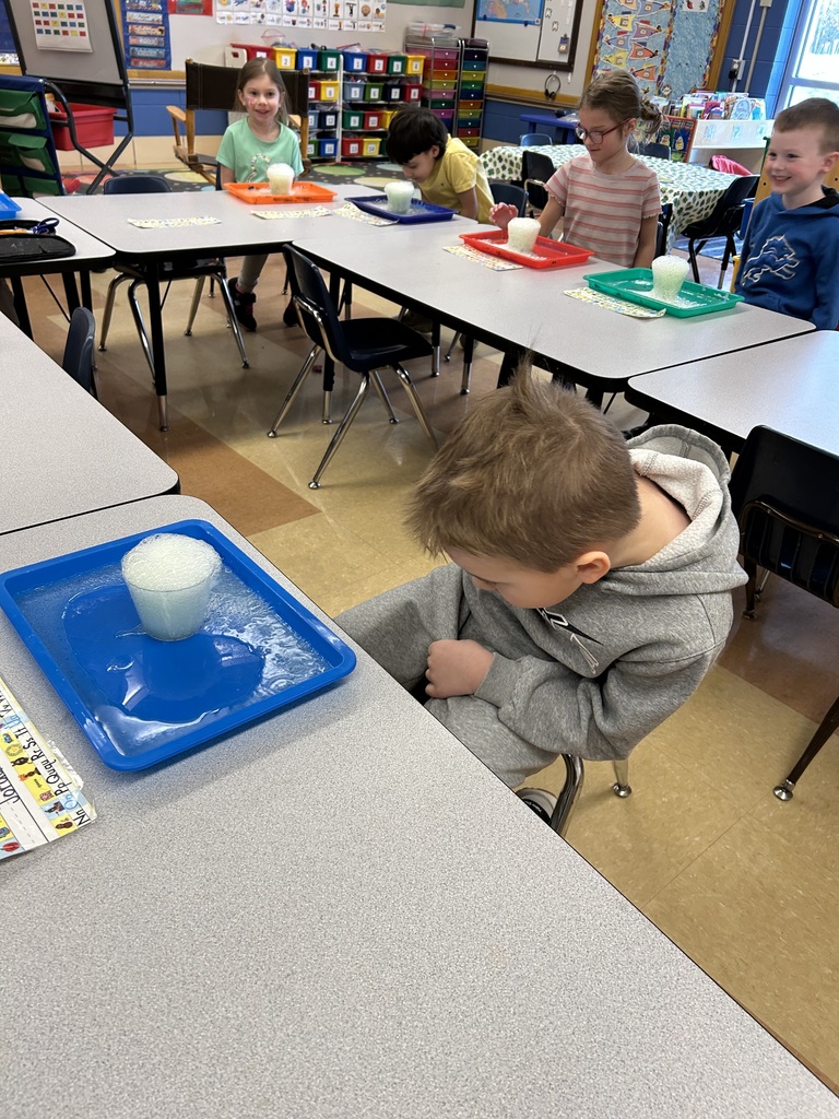students watching a science experiment with a cup of bubbling solution sitting on their desk
