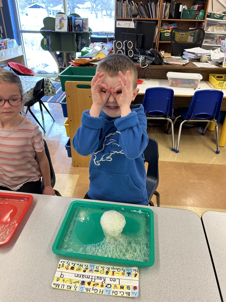 a student watching a science experiment with a cup of bubbling solution sitting on his desk