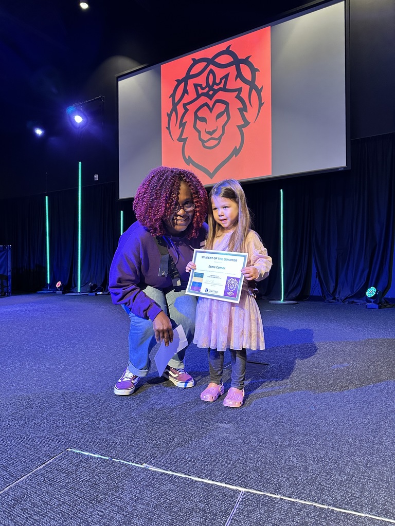 preschool student holding a certificate she was awarded and her teacher standing next to her