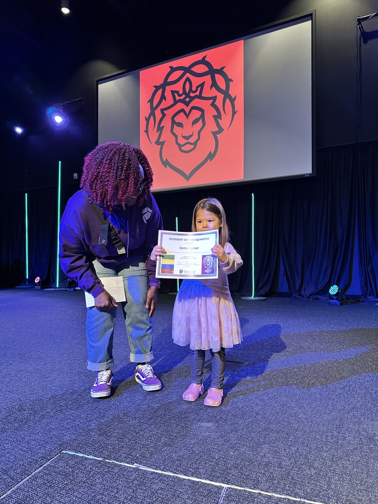 preschool student holding a certificate she was awarded and her teacher standing next to her