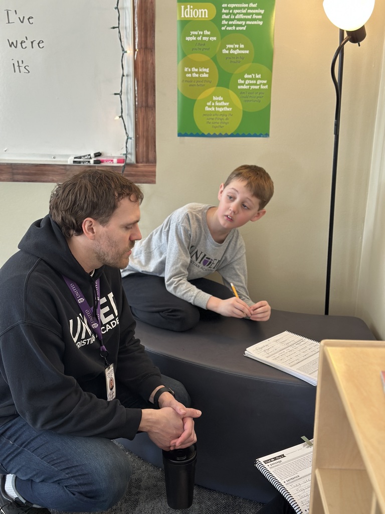 teacher crouched down next to a student while he works on an assignment