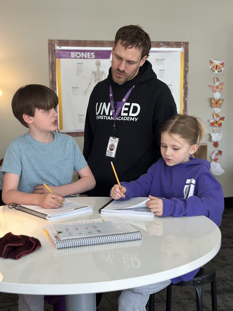two students sitting at a table working on a project with their teacher standing behind them