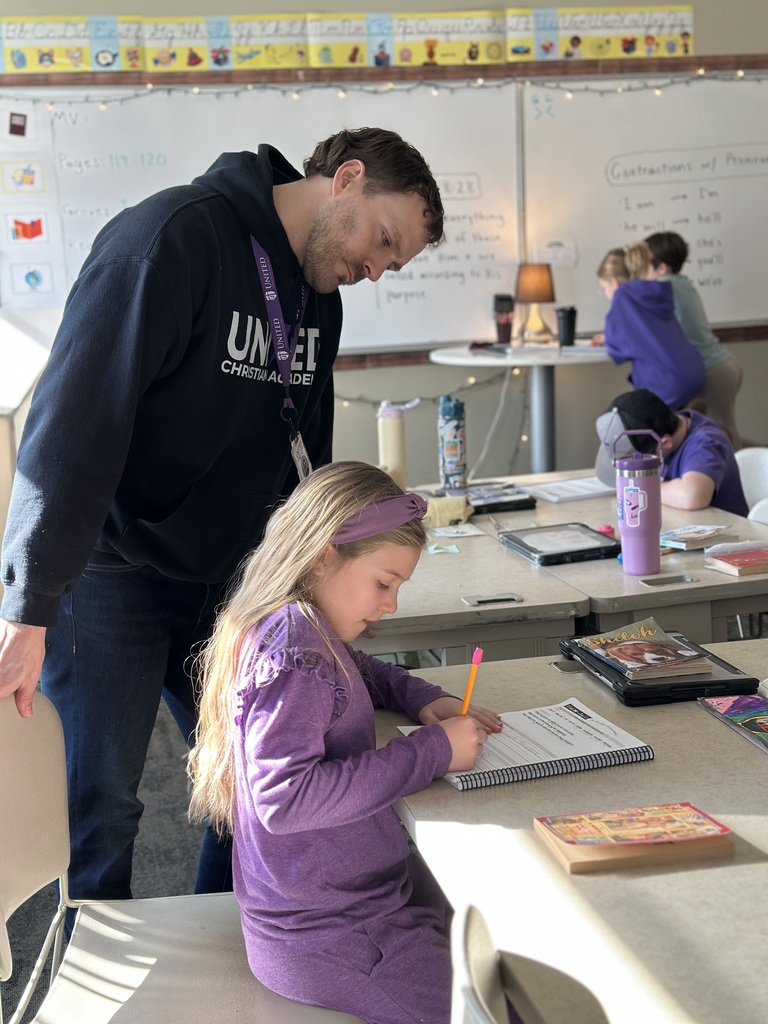 teacher standing next to a student at her desk, looking at her work