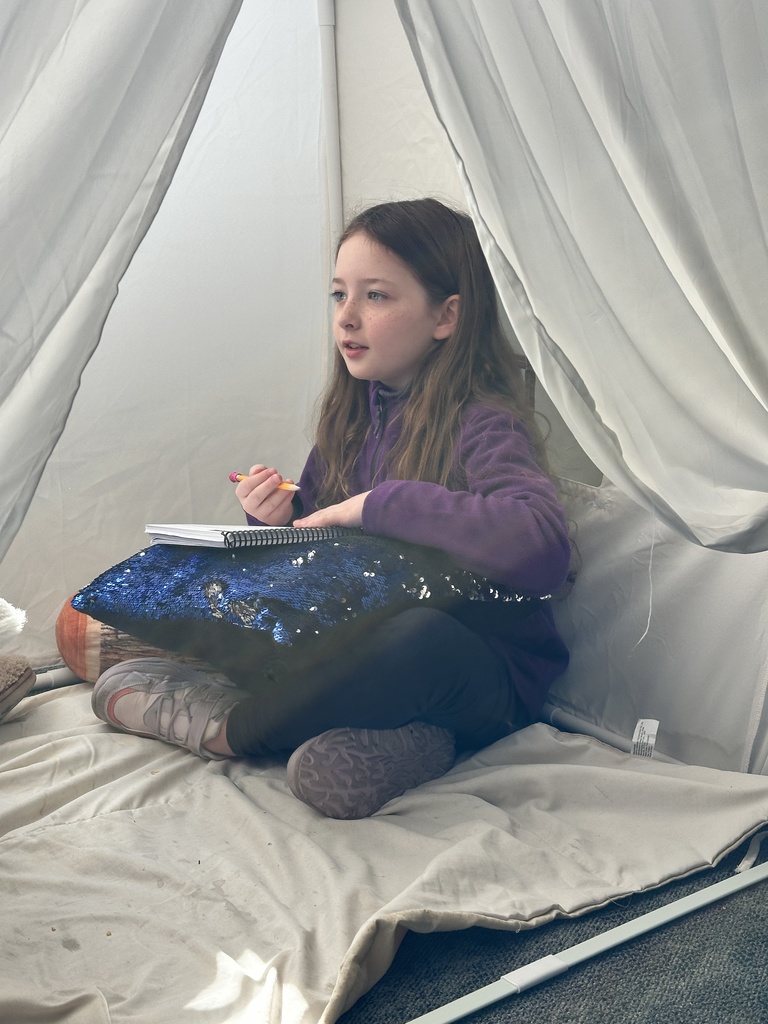 student sitting in a reading tent working on school work