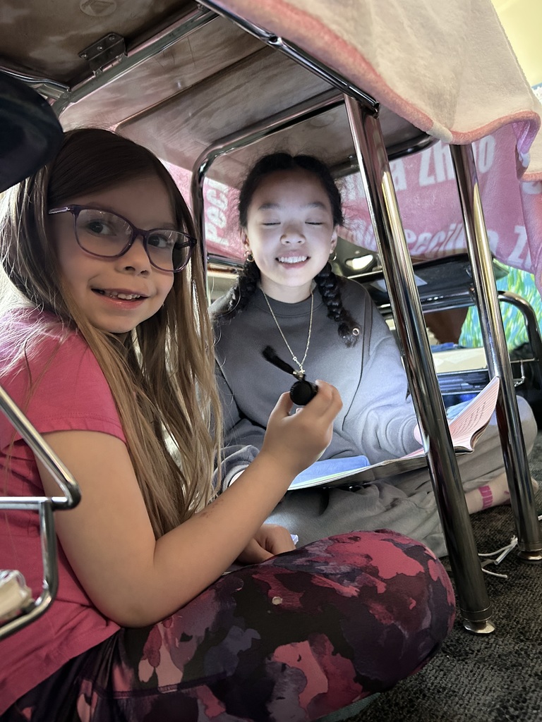 5th grade and kindergarten students reading books together by flashlight