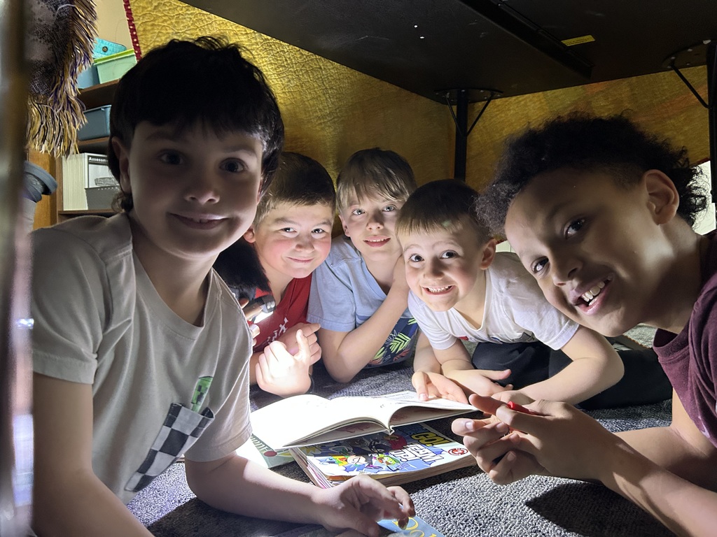5th grade and kindergarten students reading books together by flashlight