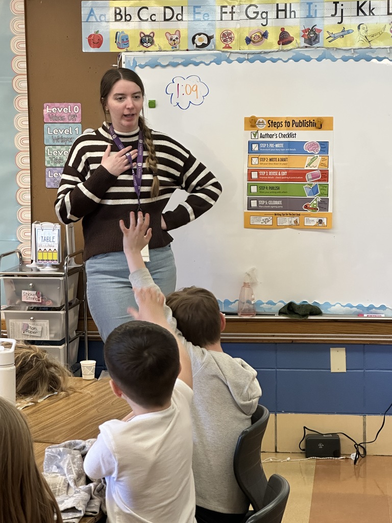 Student in front of the classroom with students raising their hands
