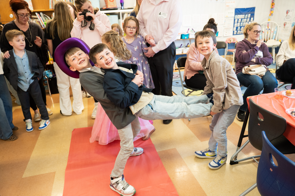 two 1st grade students holding up another student