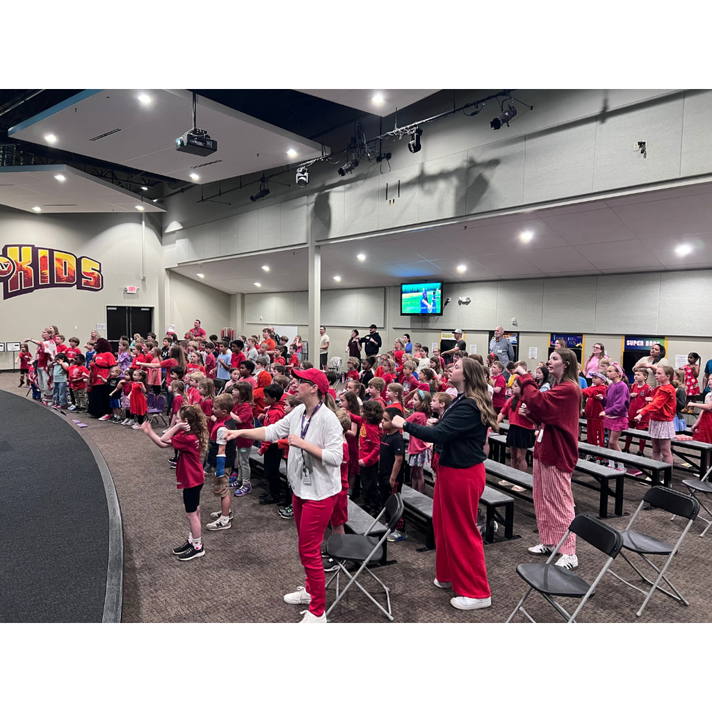 elementary students singing songs in a chapel service while wearing red