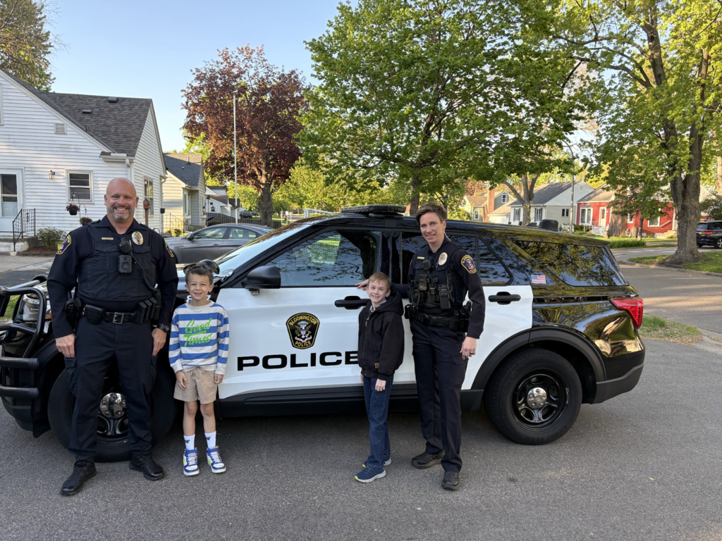 two students and two officers standing next to a police car
