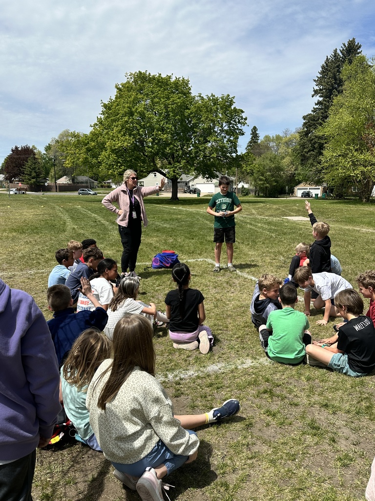 PE students sitting on the grass with teacher talking to them