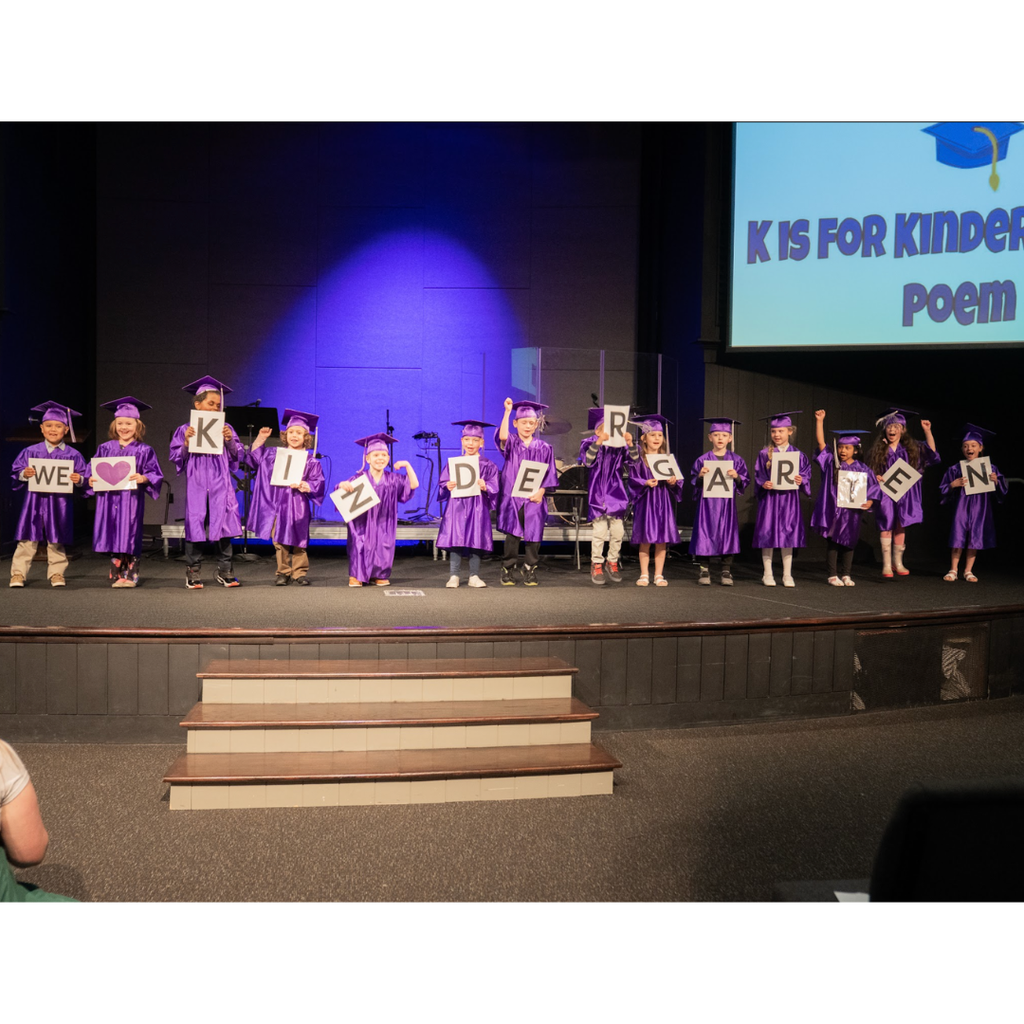 kindergarten students in caps and gowns on stage during their graduation ceremony