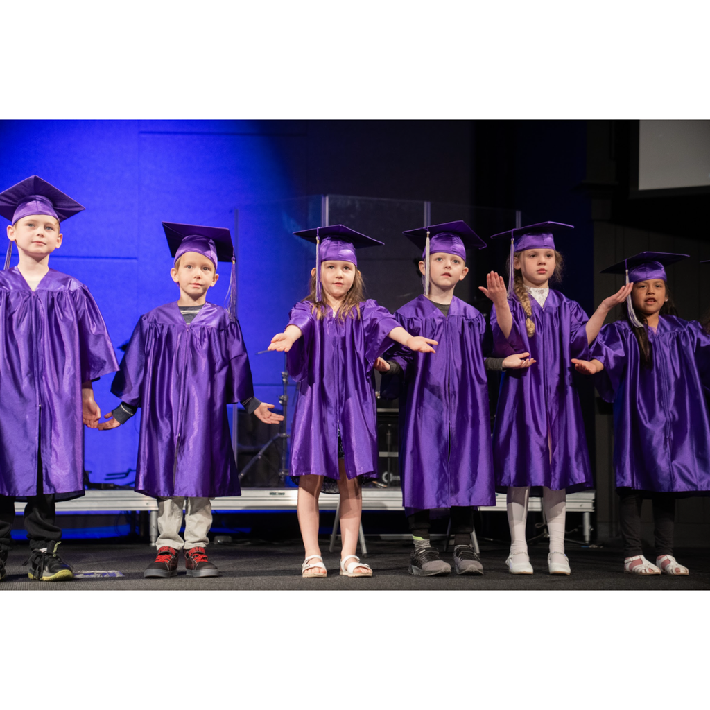 kindergarten students in caps and gowns on stage during their graduation ceremony