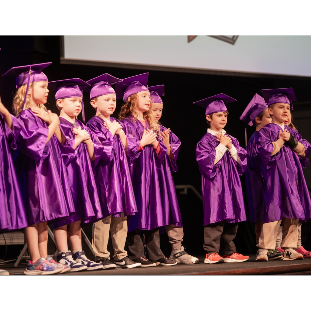 kindergarten students in caps and gowns on stage during their graduation ceremony