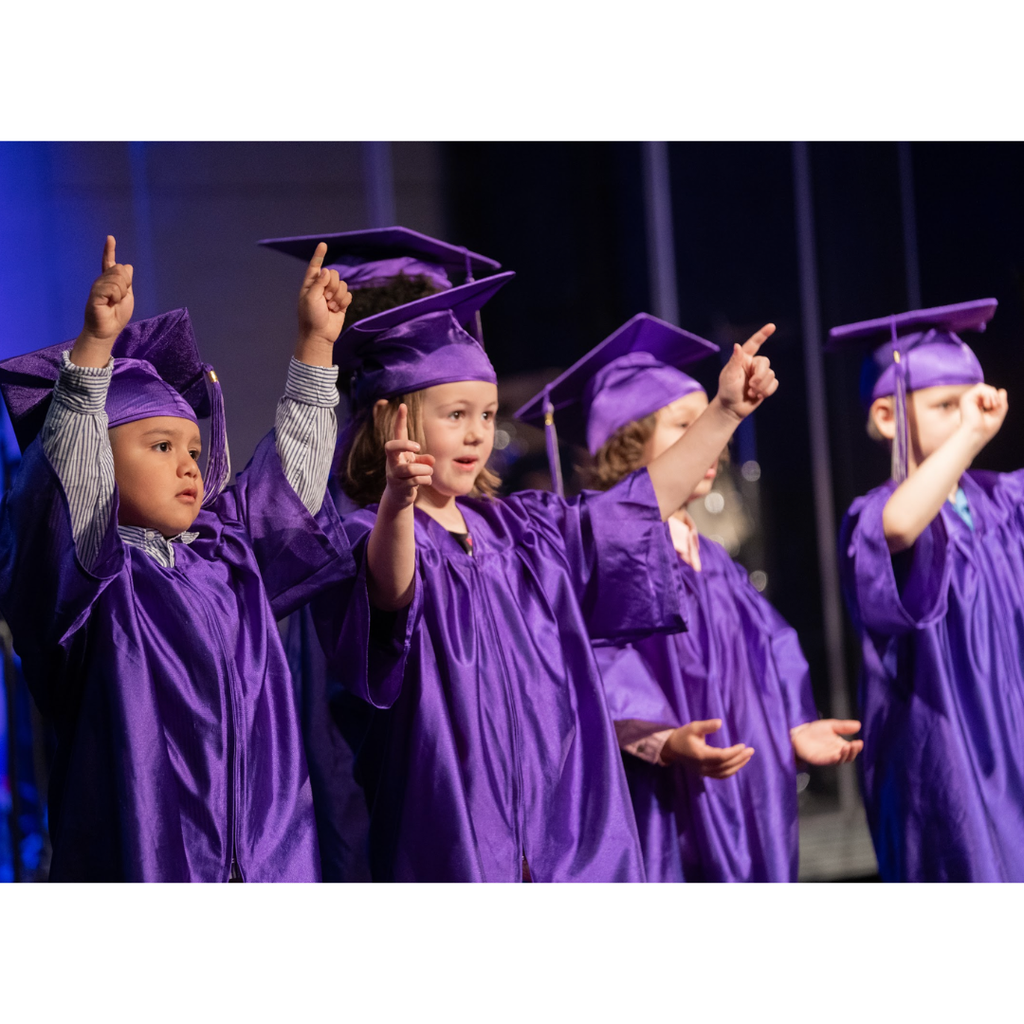 kindergarten students in caps and gowns on stage during their graduation ceremony