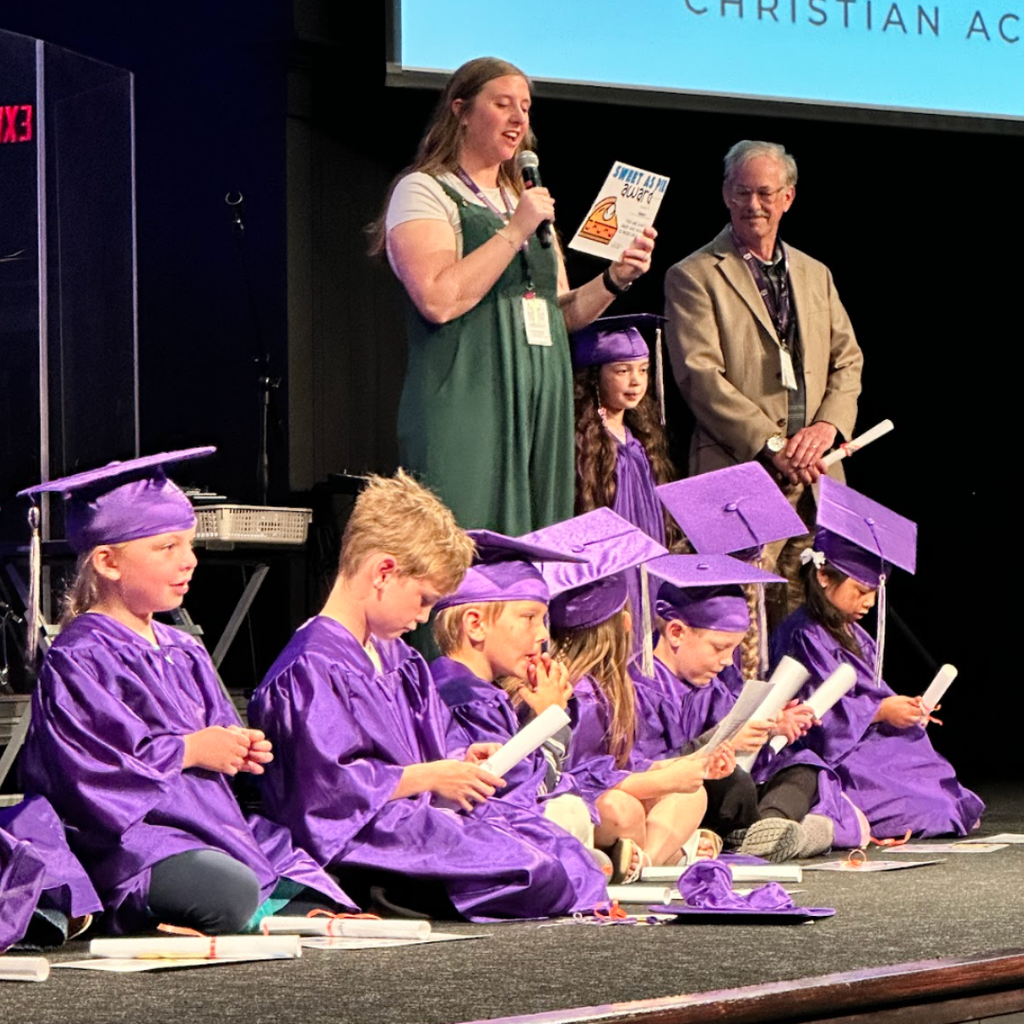 kindergarten students in caps and gowns on stage during their graduation ceremony