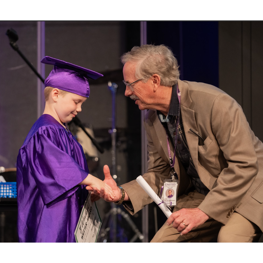 principal shaking hand of kindergarten student during graduation ceremony