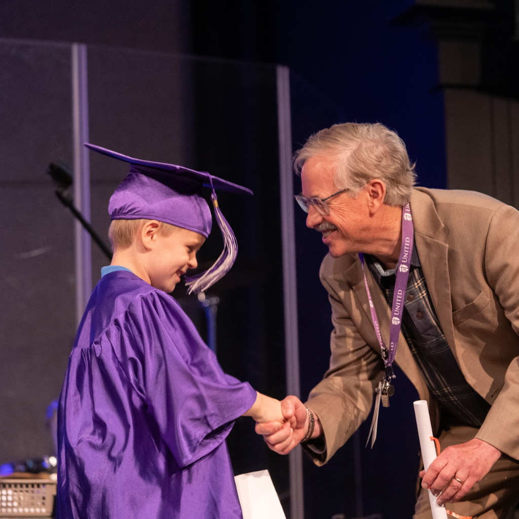 principal shaking hand of kindergarten student during graduation ceremony