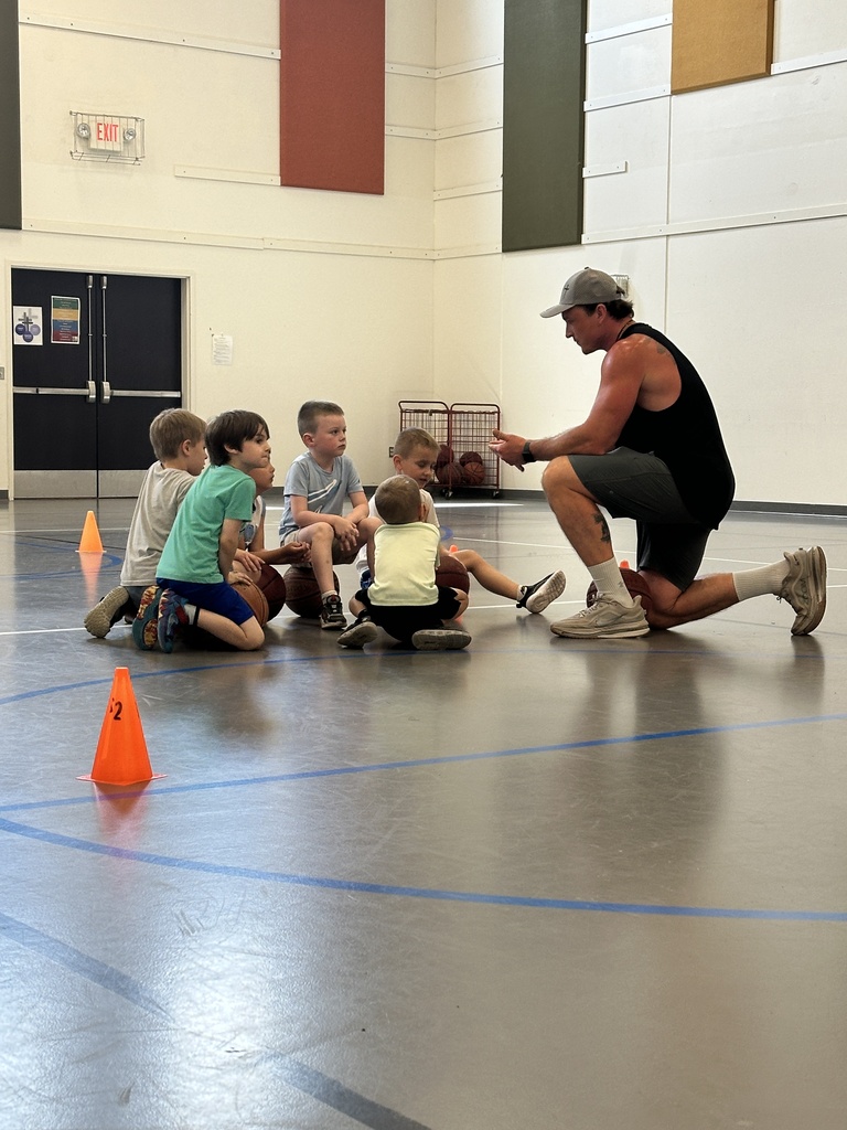 coach kneeling on the gym floor talking to young boys sitting around him