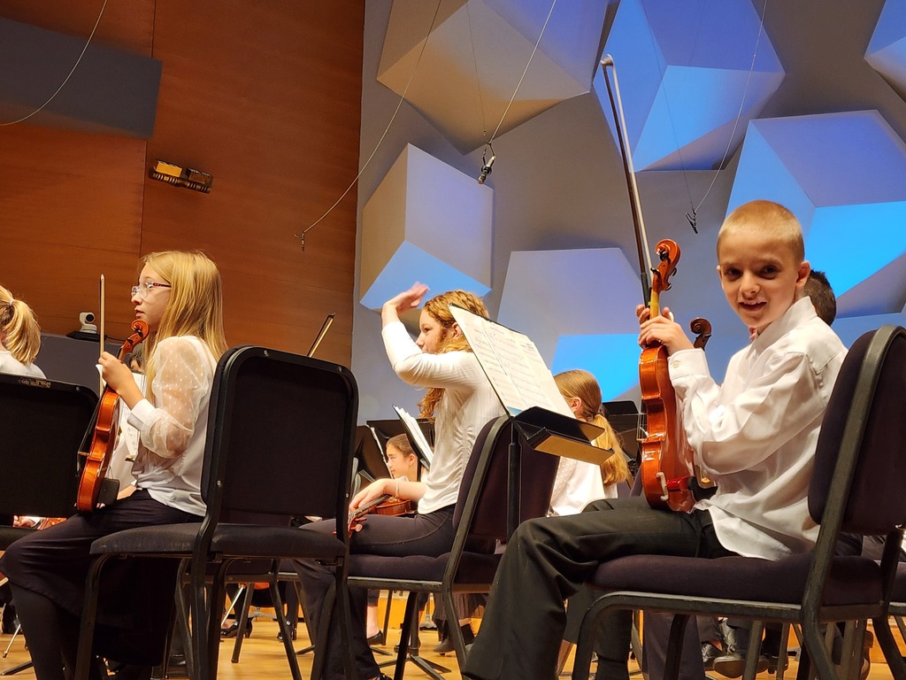 student sitting on stage with an orchestra holding a violin