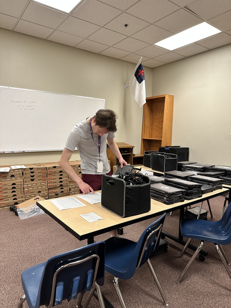 man looking at a list of names and a pile of chromebooks