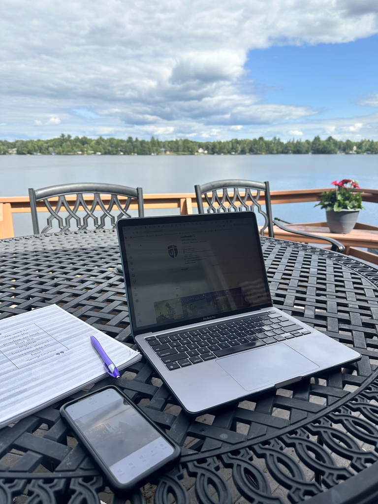 laptop and a notebook on a table overlooking a lake