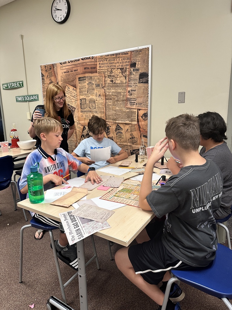 students sitting at a table trying to solve puzzles with a teacher looking over their shoulder