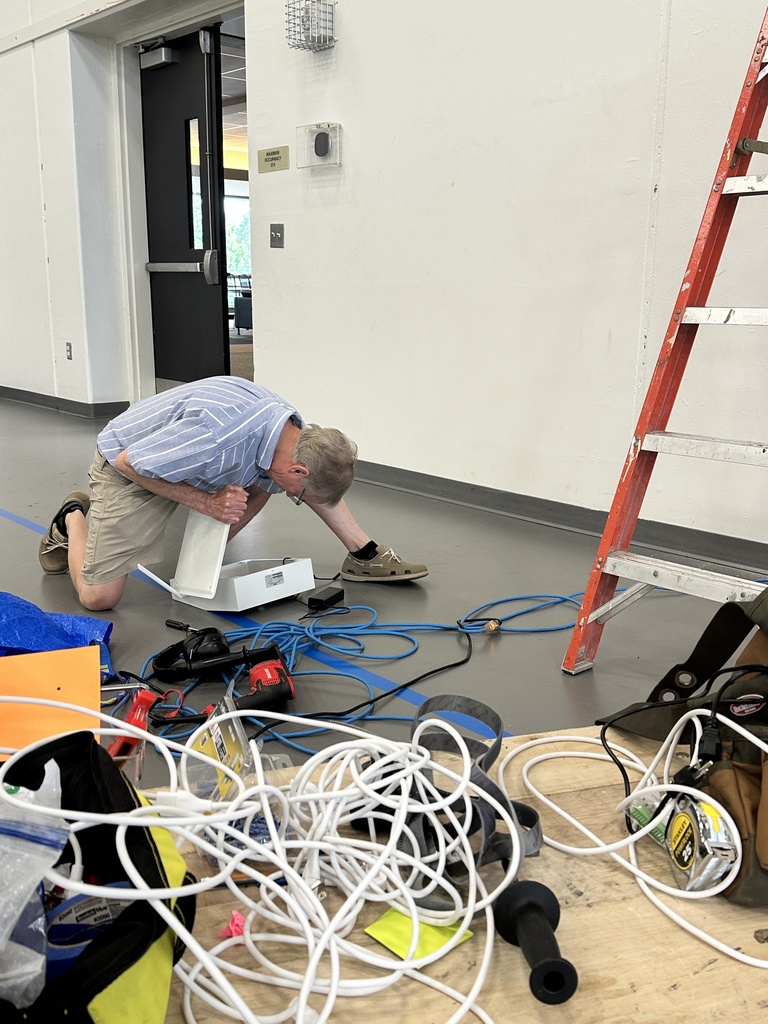 teacher kneeling on the ground working on wiring of a new intercom system