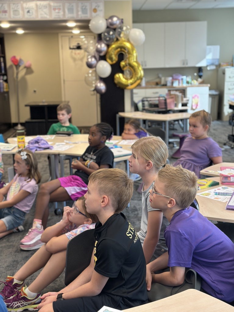 students in a classroom listening to a teacher read a book