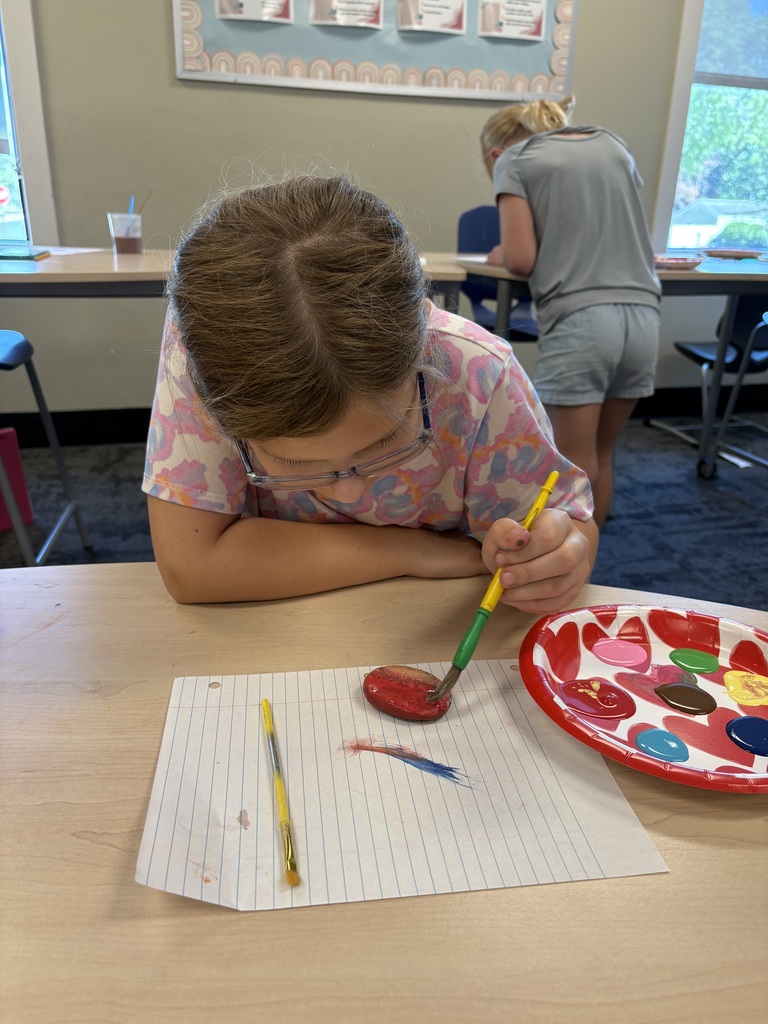 student painting a rock at her desk