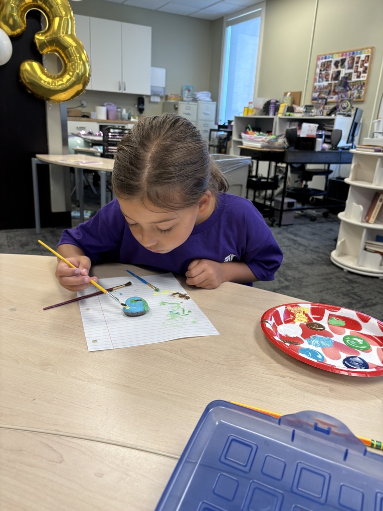 student painting a rock at her desk