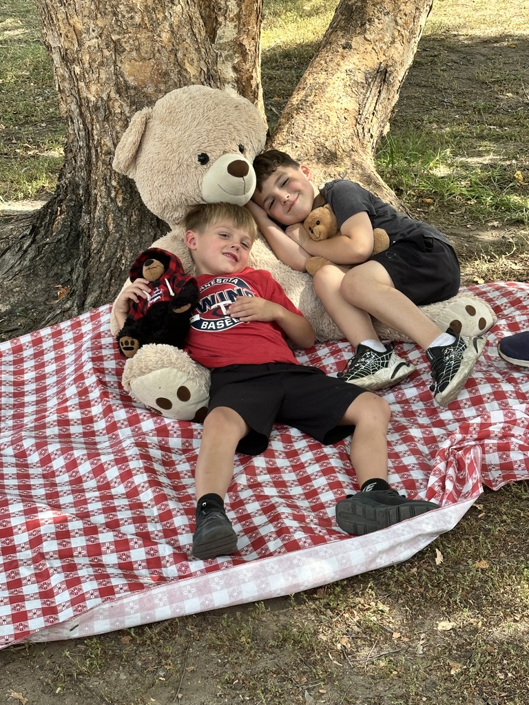students sitting on a picnic blanket with a large teddy bear