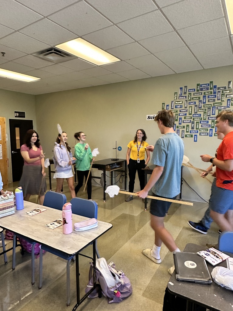 high school students in a classroom holding stick horses and pieces of paper
