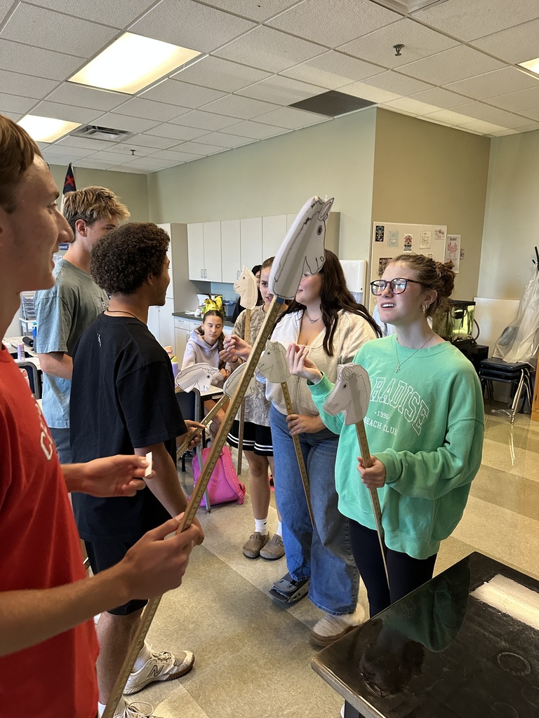 high school students in a classroom holding stick horses and pieces of paper