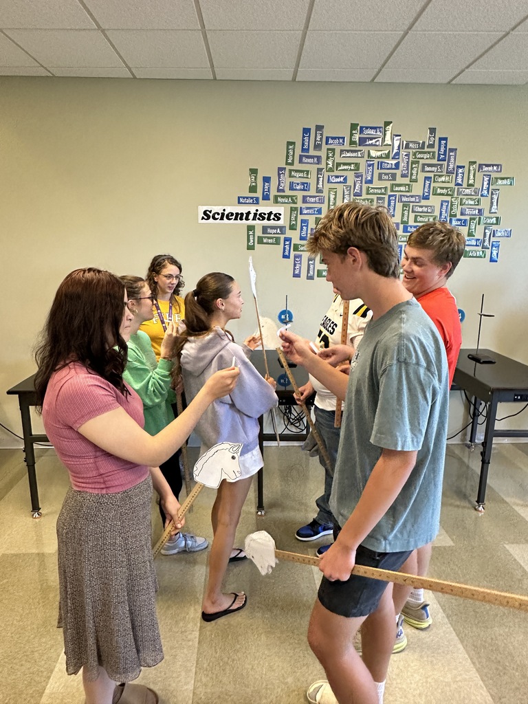 high school students in a classroom holding stick horses and pieces of paper