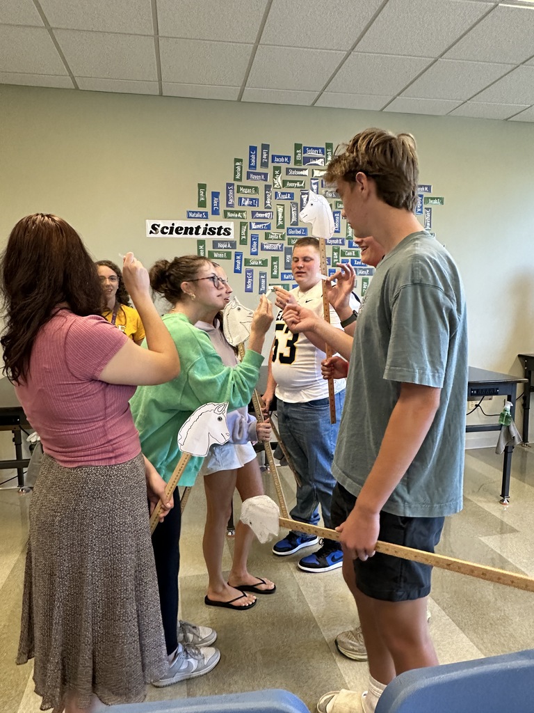 high school students in a classroom holding stick horses and pieces of paper