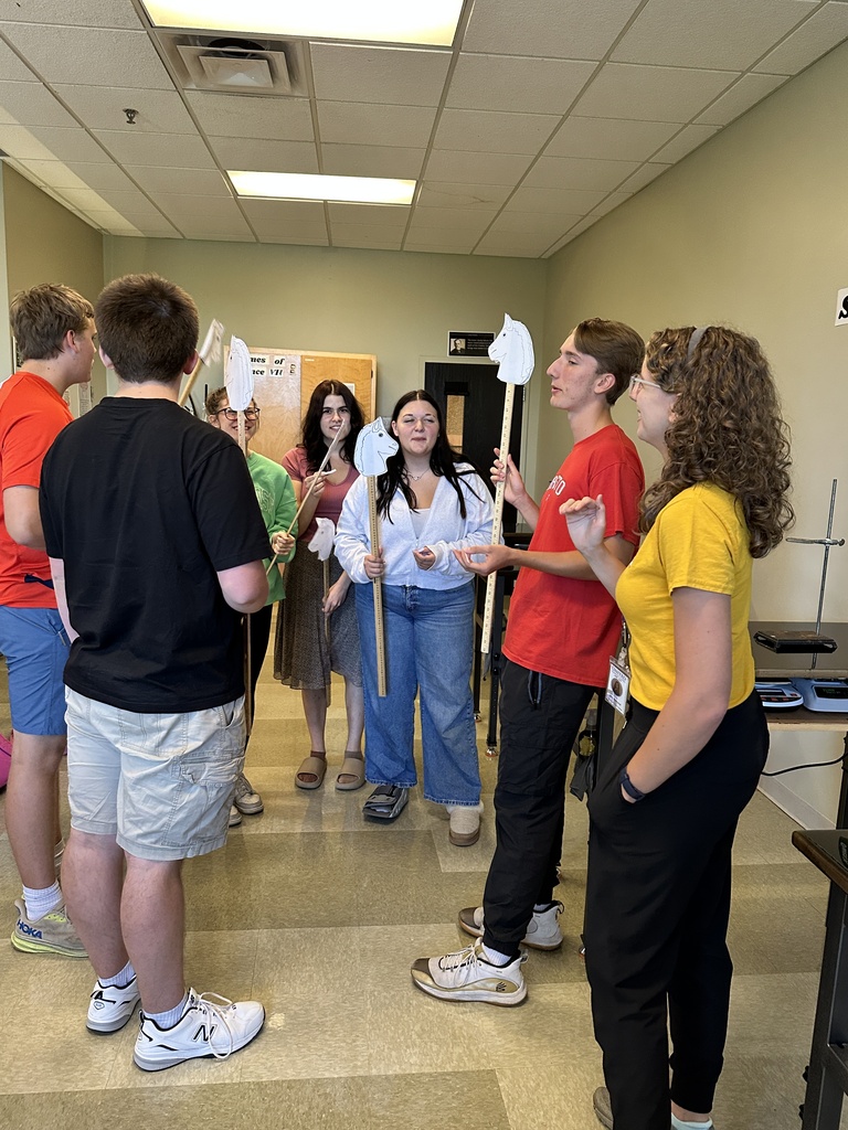high school students in a classroom holding stick horses and pieces of paper