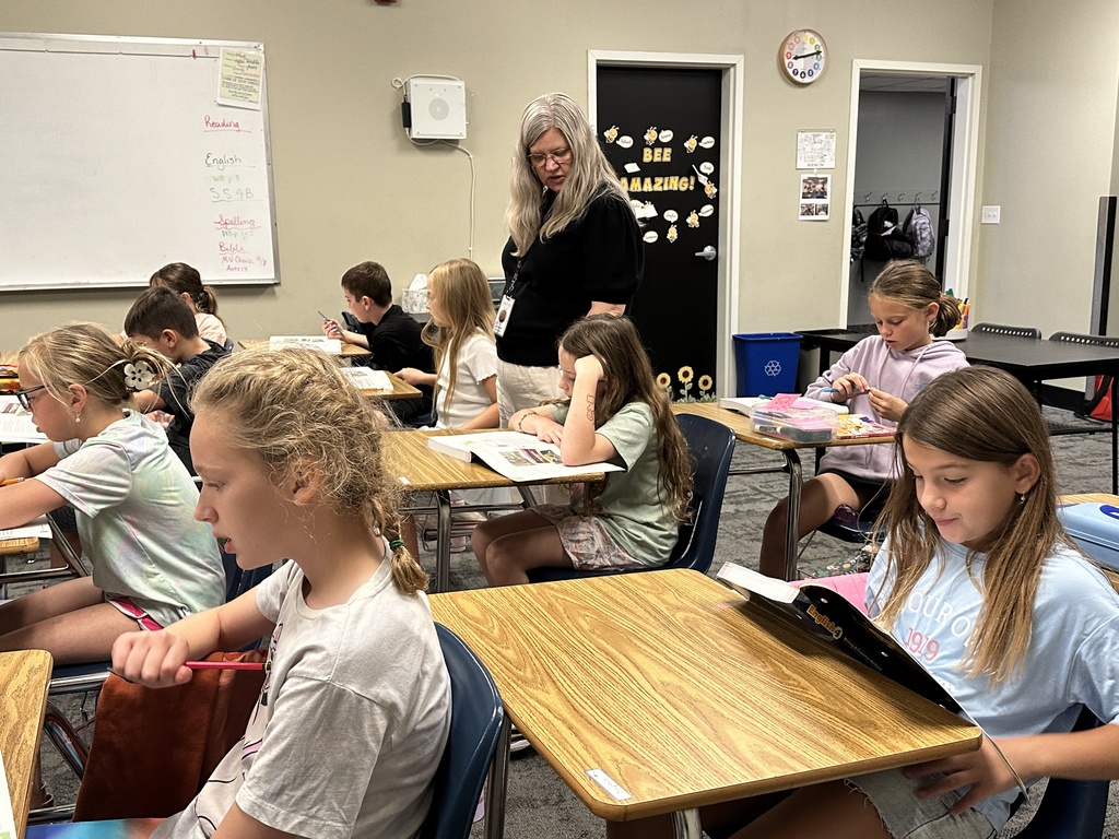 teacher walking around classroom helping students at their desk