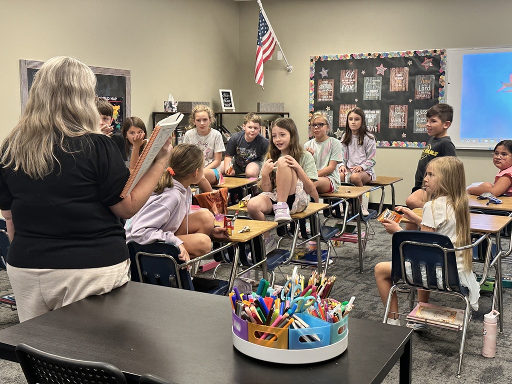 teacher at her desk and students at their desks looking at the teacher