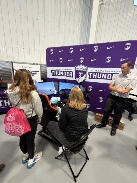man standing next to flight simulator talking to the people using it