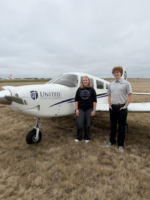 two students standing next to a small airplane