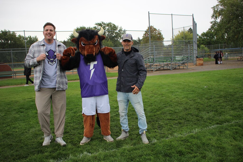 two staff members standing with the school mascot
