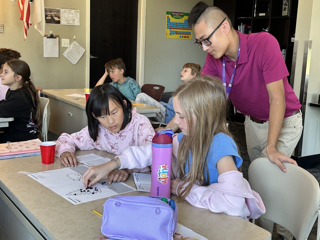 teacher leaning over a students desk to help with their work