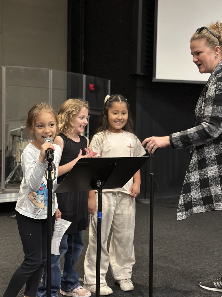 three young girls standing on stage by a music stand with microphones