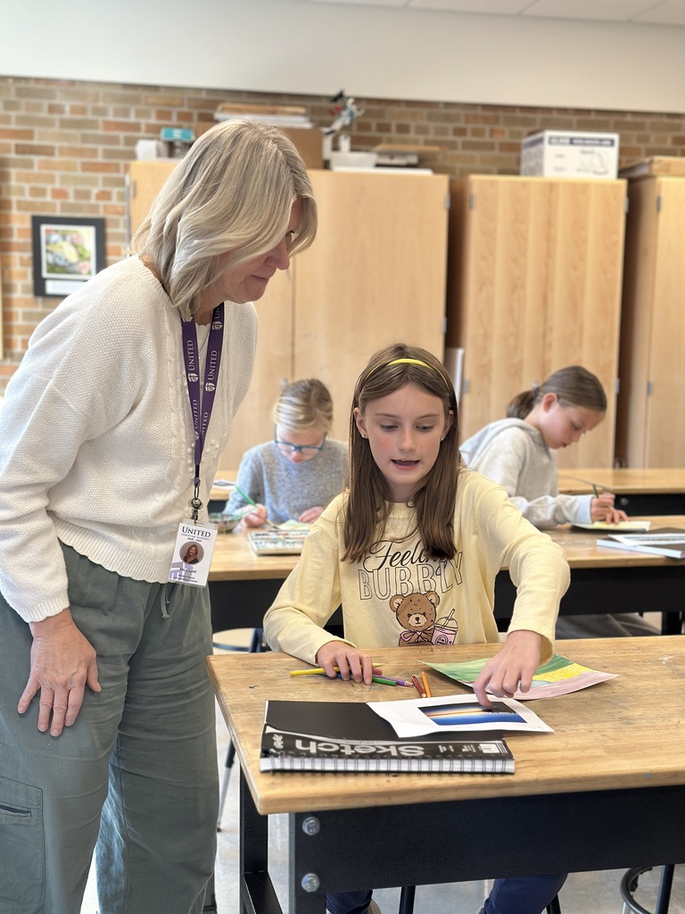 teacher helping a student at her desk with an art project