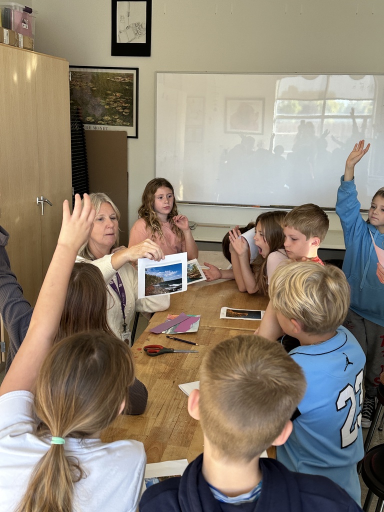 teacher holding up a piece of paper with students gathered around her looking at the paper