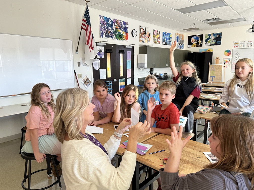 teacher holding up a piece of paper with students gathered around her looking at the paper