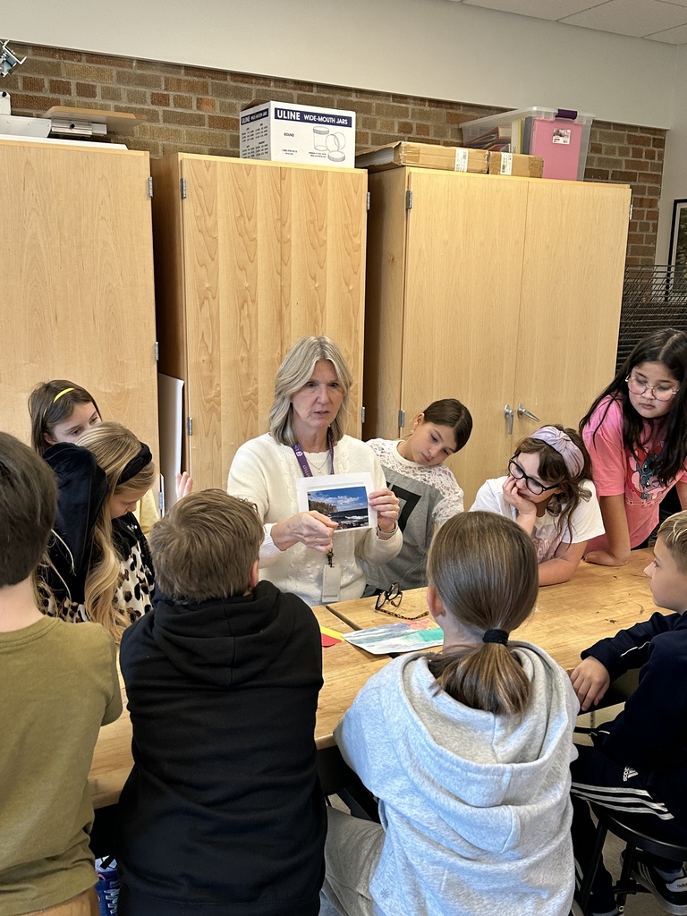 teacher holding up a piece of paper with students gathered around her looking at the paper