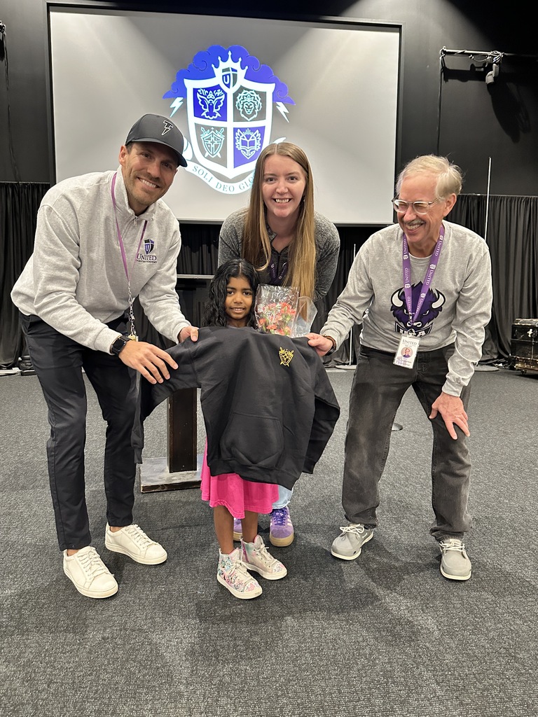 student holding a sweatshirt  and flowers with three teachers behind her
